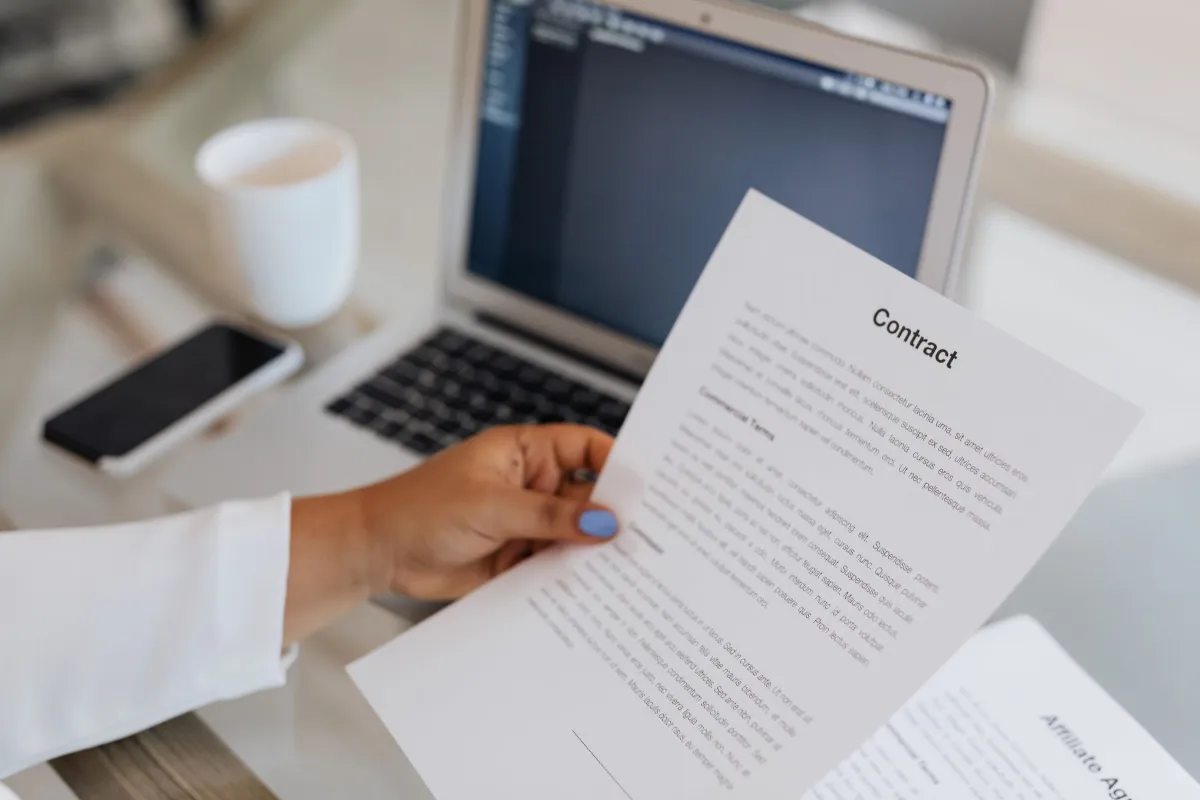 A person holding a printed job contract next to a laptop and a cup of coffee