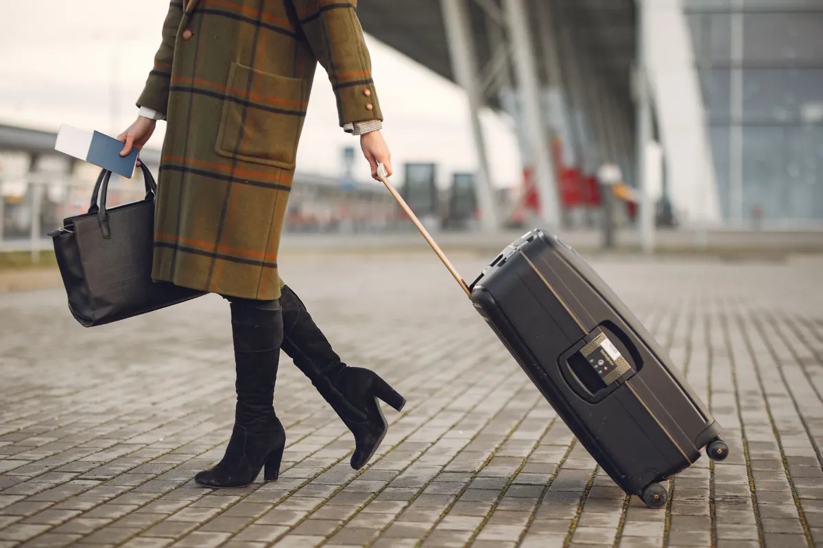 A traveller walking with a suitcase and travel documents outside an airport terminal